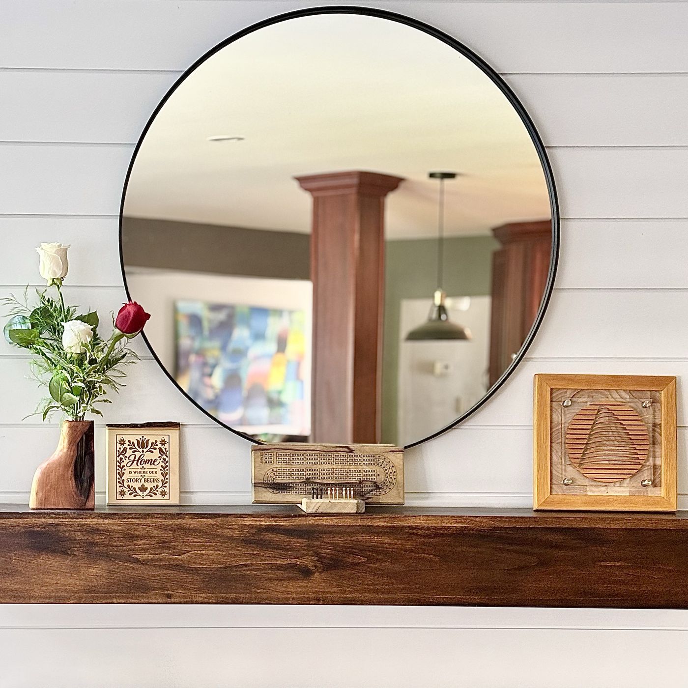 Vase woodvase avec roses sur un manteau de foyer en bois, sous un grand miroir rond